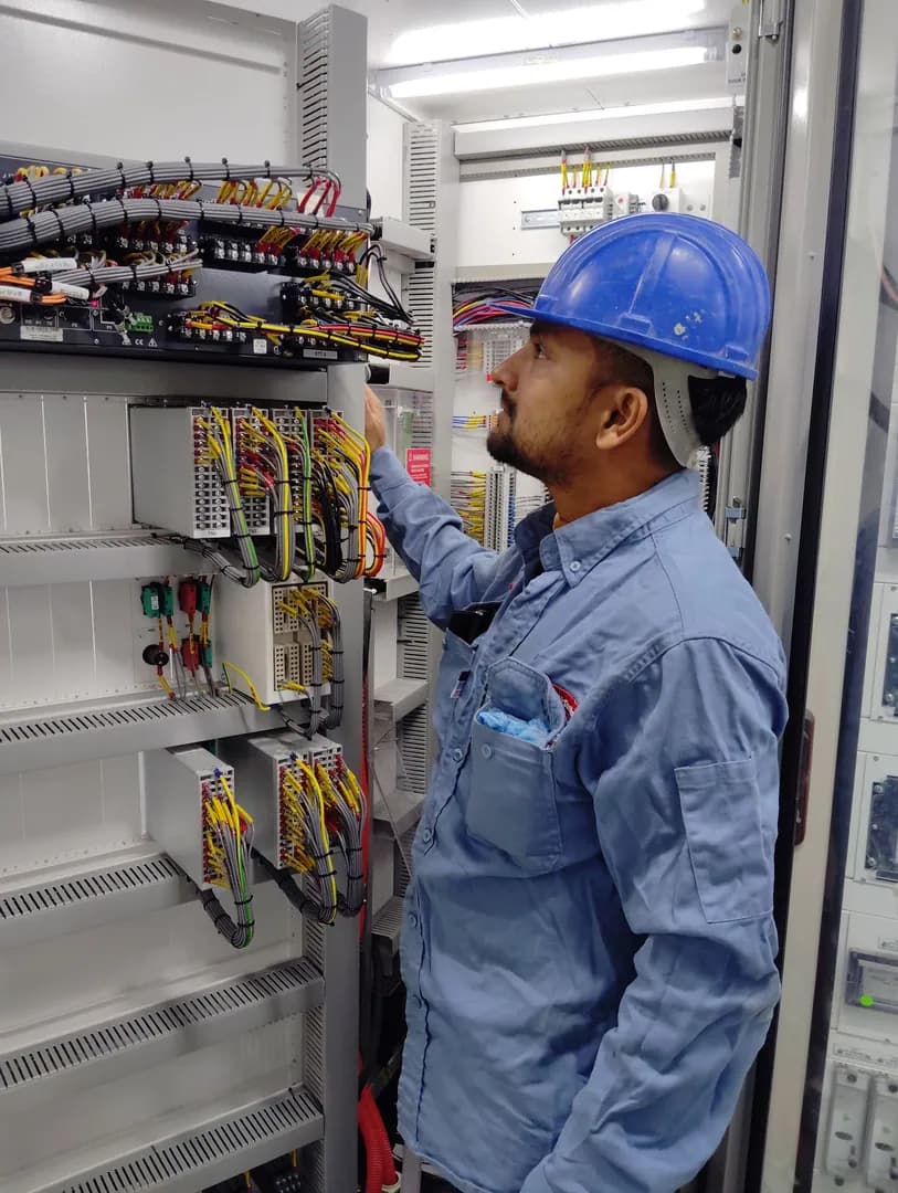 Professionnel portant un casque bleu devant les câbles et composants d’une armoire électrique