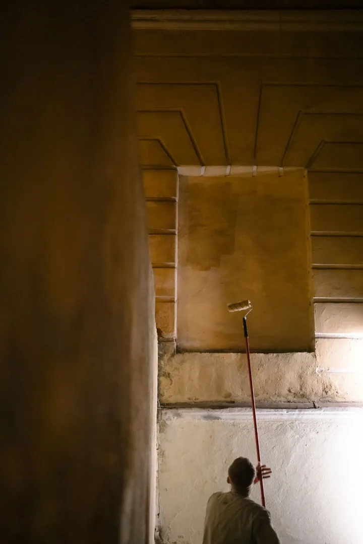 Vue de dos d’une personne peignant un mur intérieur avec un rouleau