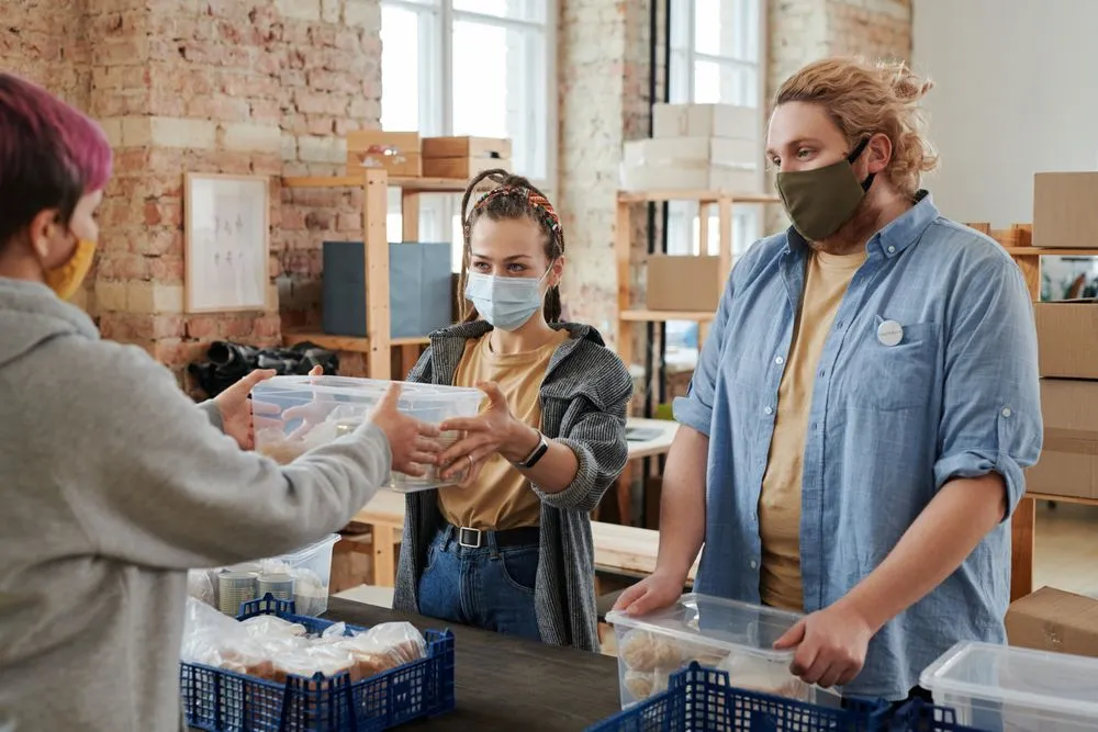 Des bénévoles masqués réceptionnent des dons alimentaires dans des boîtes lors d’une collecte solidaire