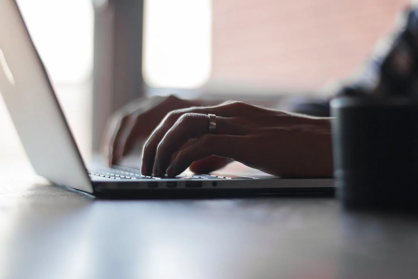 Des mains travaillent sur le clavier d’un ordinateur portable près d’une fenêtre.