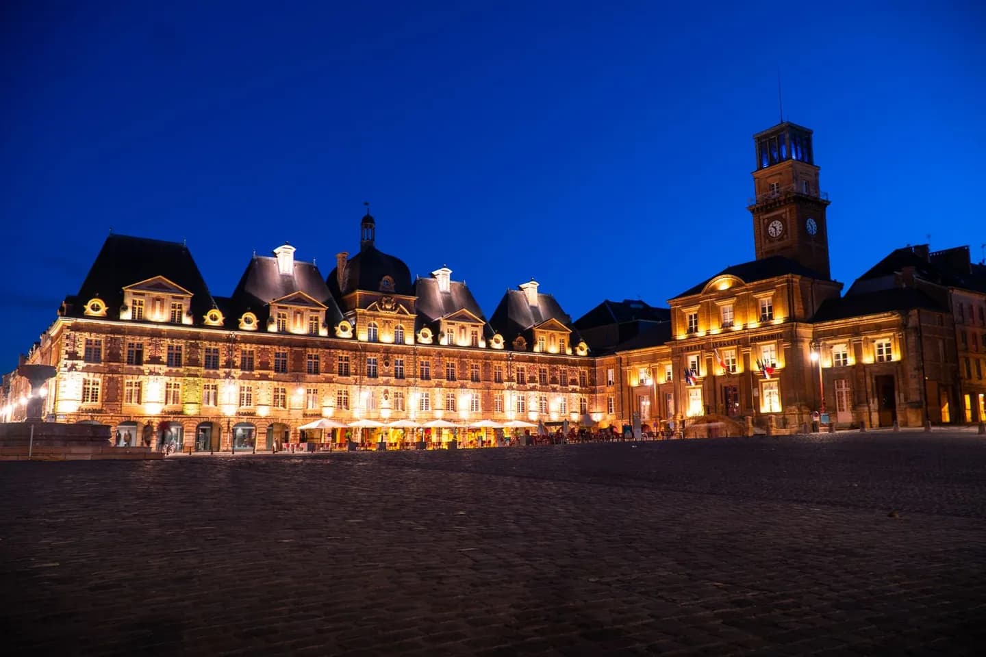 Place pavée et hôtel de ville illuminé à la tombée du jour en France
