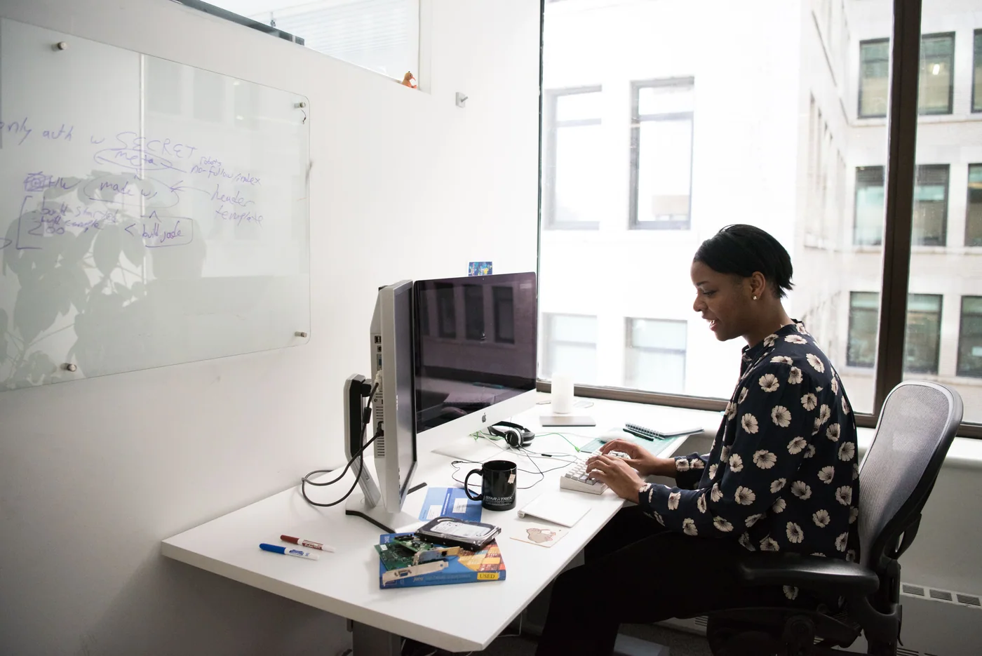 Une femme utilise un clavier devant un ordinateur de bureau, près de grandes fenêtres