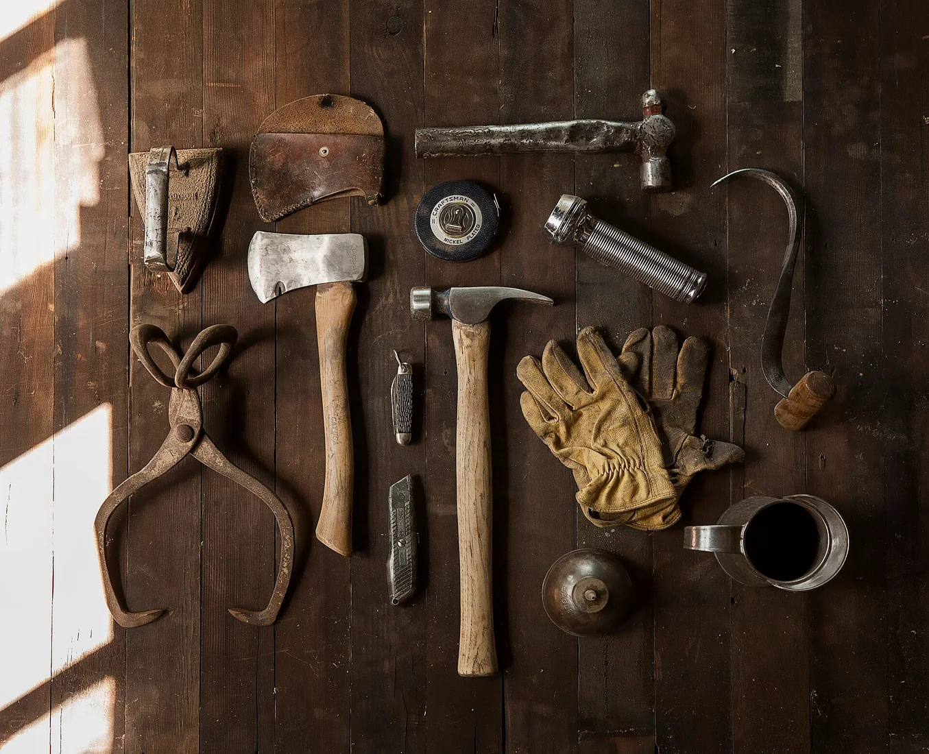 Des outils à main disposés à plat : marteau, hachette, cutter et lampe