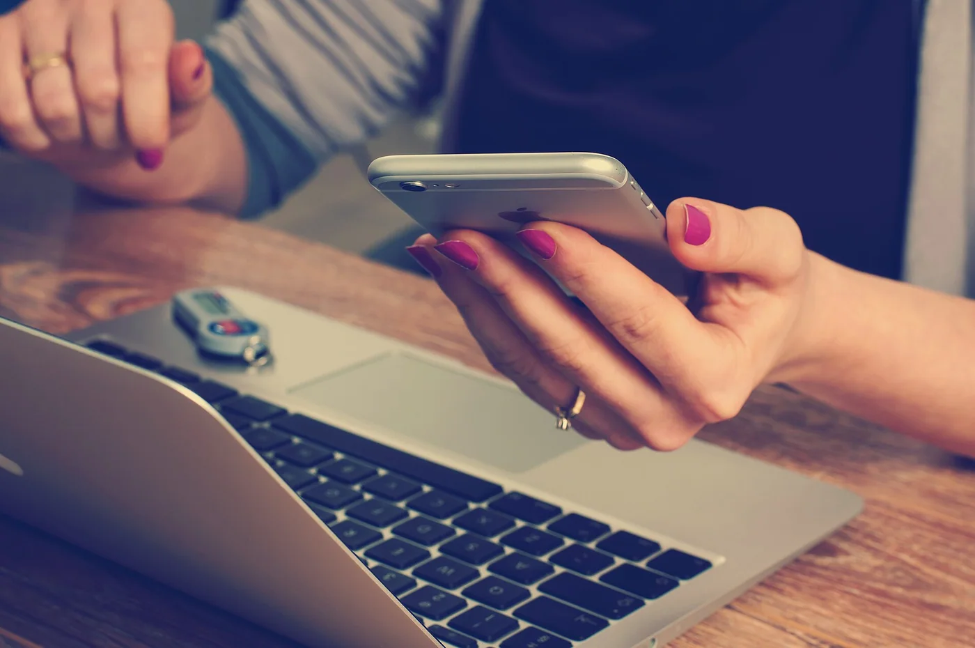 Des mains tiennent un smartphone devant un ordinateur portable