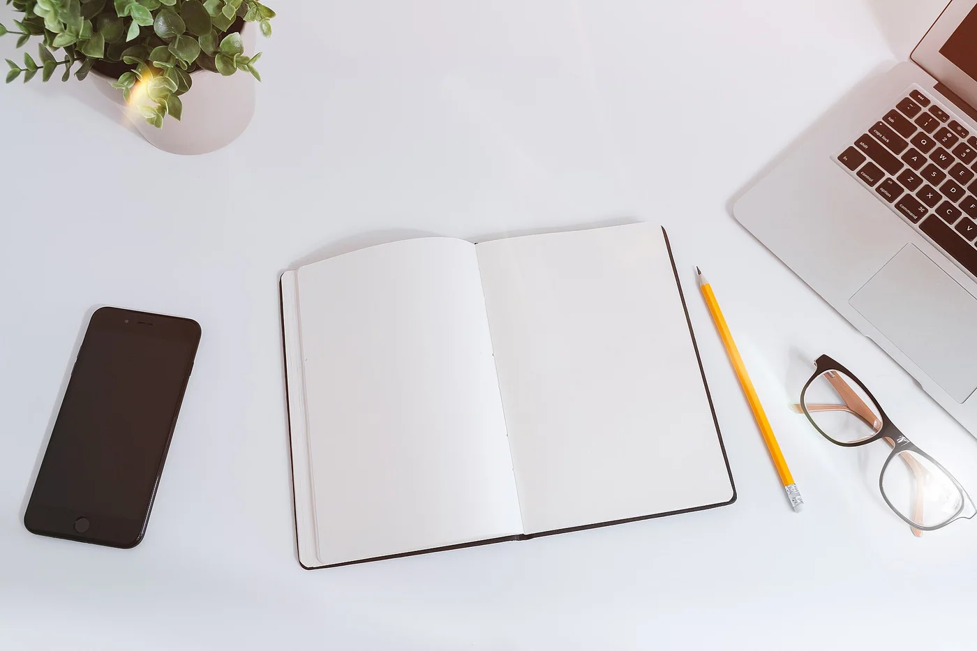 Un carnet ouvert, un ordinateur et un téléphone sur une table blanche